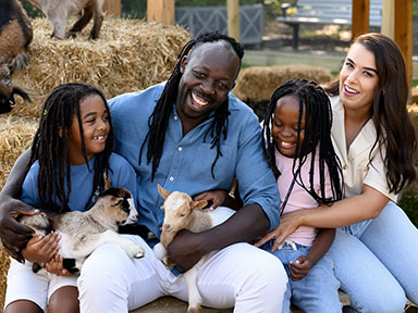 A family of four seated on hay bales cuddle baby goats at the Sydney Royal Easter Show's Farmyard Nursery.