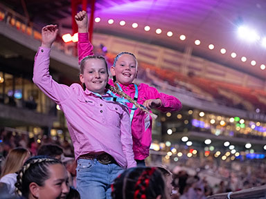 Two young girls in pink clothing cheer with raised arms from reserved seats at Sydney Royal Easter Show's Evening Entertainment event.